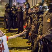 Un jeune homme, à genoux, tenant une pancarte « vote oui », offre un œillet à des policiers espagnols (Àngel García)